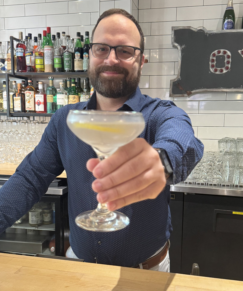 Patrick standing behind bar at Lupo holding a hand crafted cocktail